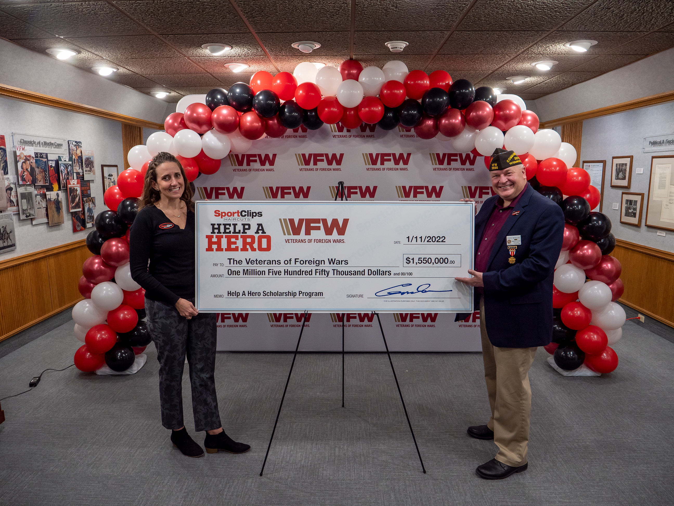 A Sport Clips team member and a veteran hold a large check from Sport Clips Haircuts to the VFW - Veterans of Foreign Wars