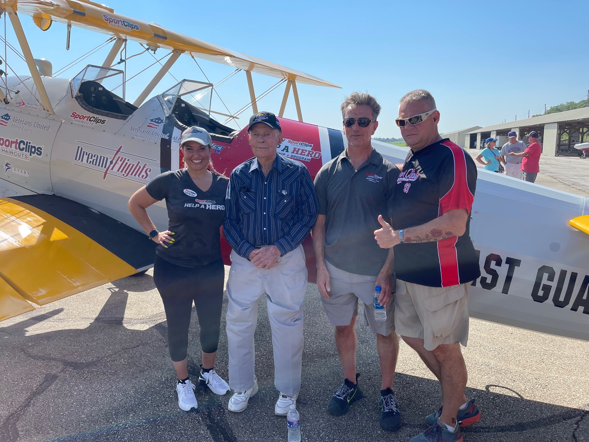 Sport Clips logo on a Dream Flights biplane with a veteran, a pilot and Sport Clips team members in front of it